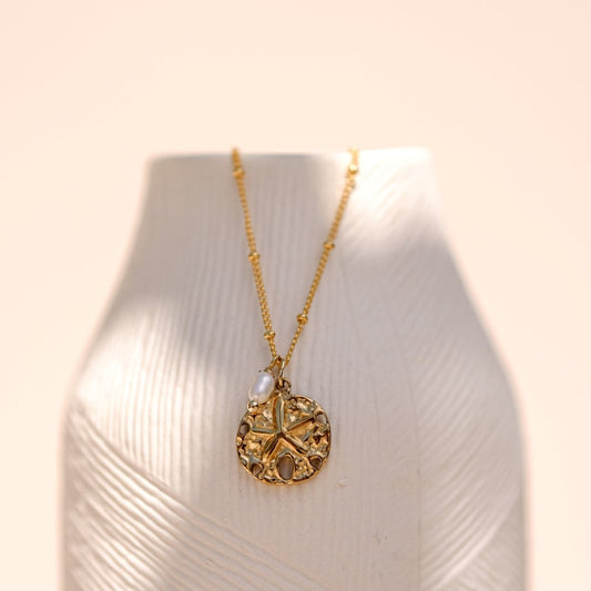 Collier "Adventure" composé d'une médaille "Sand Dollar" accompagné d'une perle de culture blanche monté sur une chaine fine à bille le tout doré à l'or fin.